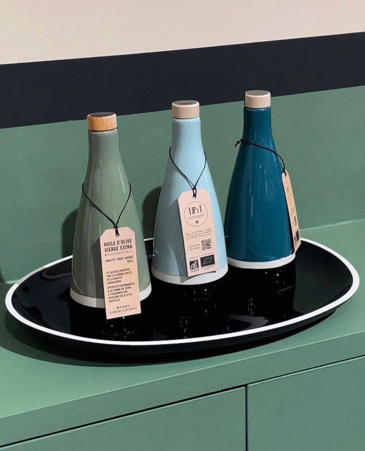 3 bouteilles en céramique verte, bleu ciel et bleu turquoise avec un liseret blanc et noir sont sur un plateau noir
