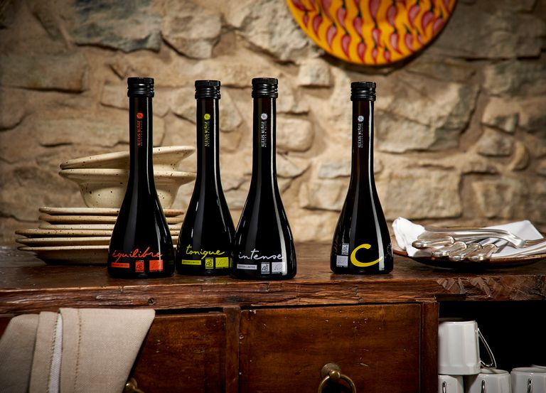 Bouteilles en verre d'huiles d'olive Editions Limitées, de la marque Alexis Muñoz, posées sur un buffet en bois avec des assiette et des couverts en argent.