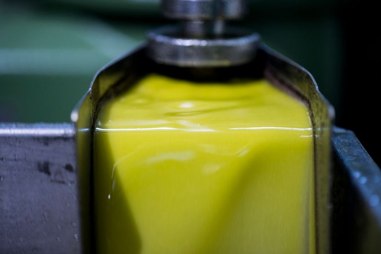 Gros plan sur de l'huile d'olive fraîche jaune-vert s'écoulant d'un bec en métal lors du processus de production, avec une surface brillante et réfléchissante et des équipements en inox en arrière-plan.