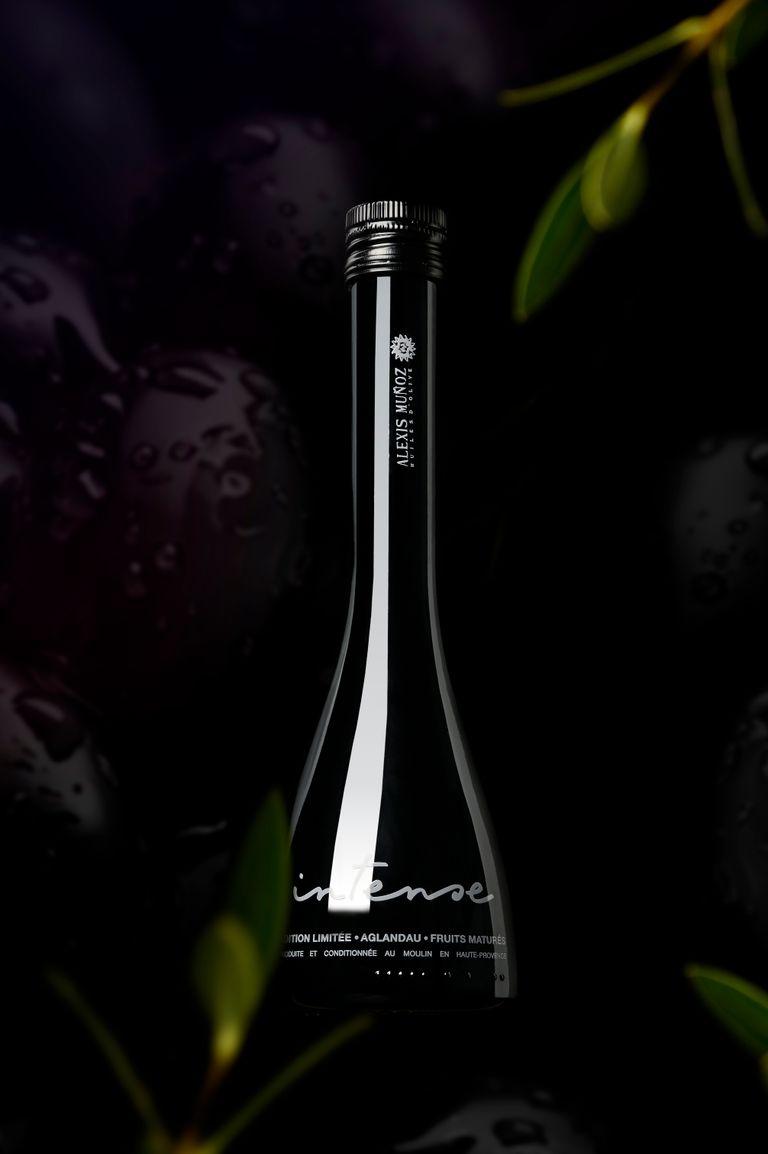 Glass bottle of Intense olive oil, limited edition, from the Alexis Muñoz brand, on a black background with olive leaves.
