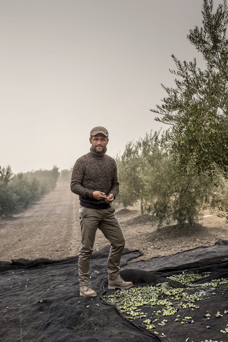 Alexis Muñoz standing beside an olive tree, holding the fruits delicately between his hands.