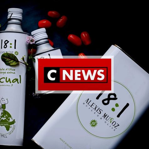 Photo d'ambiance avec des tomates et des fleurs violettes, mettant en scène des bidons carré et cylindriques de couleur blanches, d'huile d'olive 18:1 Alexis Muñoz, avec le logo CNEWS