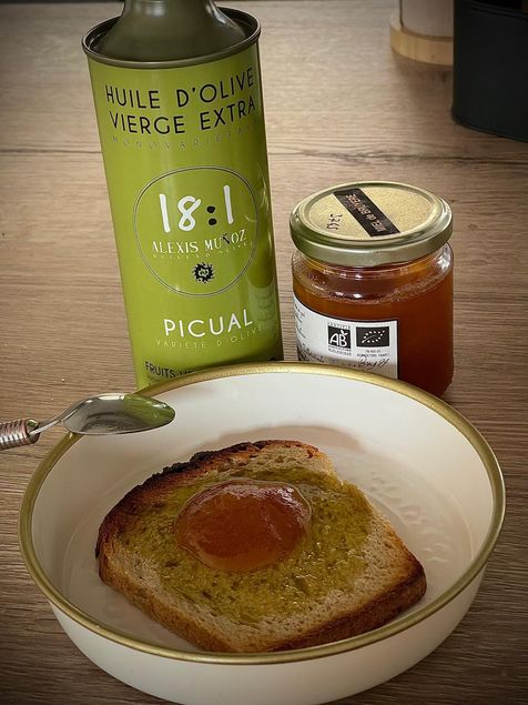 tranche de pain grillé avec de l'huile d'olive variété Picual dessus et du miel, il y a une cuillère à coté, un pot de miel et un bidon d'huile d'olive 18:1 variété Picual