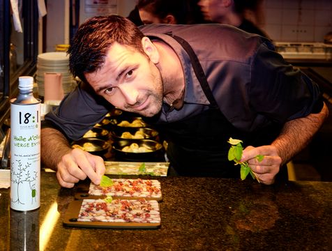 Chef Nicolas Brousse en cuisine avec des herbes aromatiques dans les mains et un bidon d'huile d'olive 18:1 variété Picual, de la marque Alexis Muñoz.