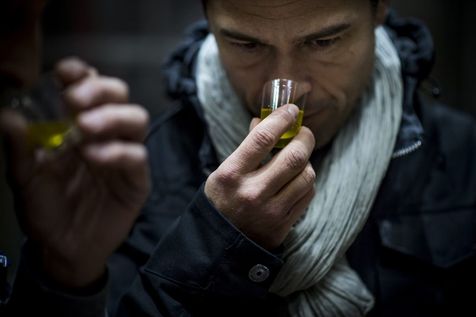 un homme a un gobelet dans sa main droite. Dans ce gobelet il y a de l'huile d'olive. L'homme sent l'huile d'olive