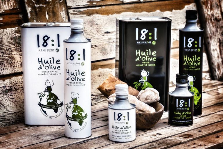 Atmospheric image of 18:1 Alexis Muñoz olive oils, cylindrical and square cans, accompanied by bread on a wooden table.