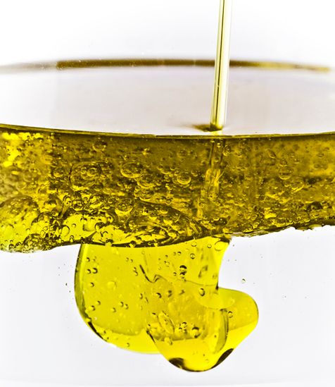 Zoom en transparence sur le mouvement de l'huile d'olive couleur jaune or, versée dans de l'eau.