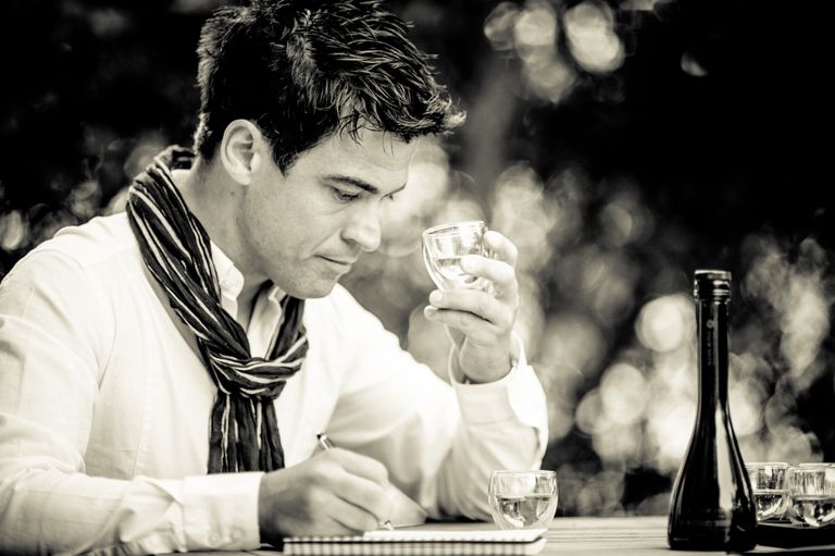 Black and white photo of Alexis Muñoz tasting olive oil while taking notes.