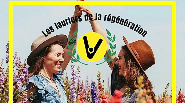 Two young girls, dressed in dresses, are holding hands and smiling at each other. They are standing in a very colorful flower field. At the center of the photo is the logo of The Laurels of Regeneration, featuring laurel leaves.