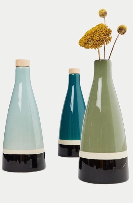 3 bouteilles en céramique bleue, verte et bleue ciel. Elles contiennent de l'huile d'olive à l'intérieur et des fleurs dans une des bouteilles