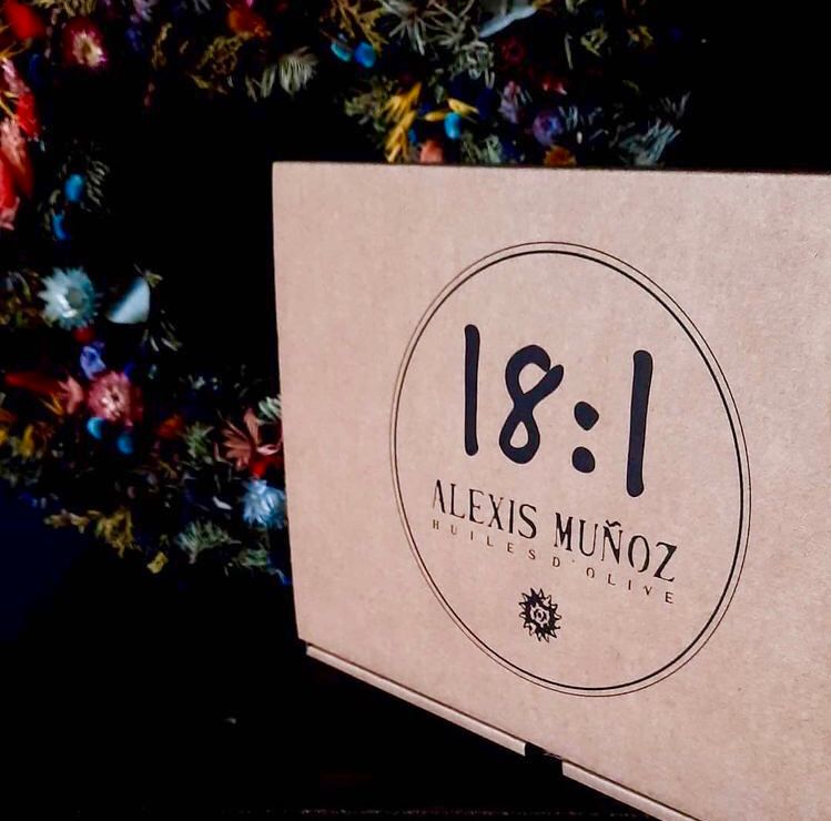 Alexis Muñoz 18:1 cardboard gift box, with a decorated Christmas tree in the background.