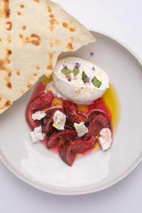Assiette colorée composée d'une buratta crémeuse, de figues roties, arrosées d'huile d'olive avec un pain pita.