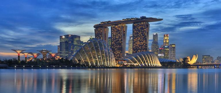Skyline of Singapore at dusk, featuring the iconic Marina Bay Sands hotel with its illuminated rooftop, the futuristic Gardens by the Bay with Supertree Grove, and the ArtScience Museum, all reflected in the calm waters of Marina Bay