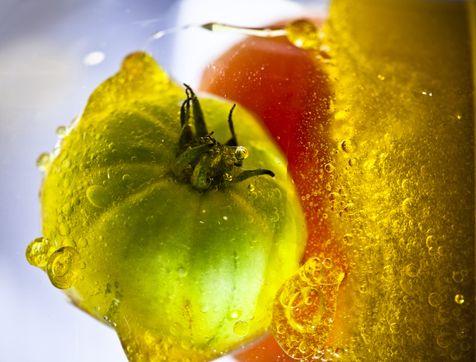 Tomates verte et rouge plongée dans l'huile d'olive en mouvement.
