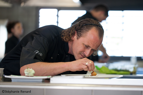 Chef Franck Renimel en train de desser attentivement une assiette dans la cuisine de son restaurant.