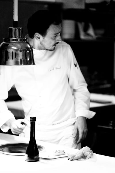Photo noir et blanc du Chef Lionel Giraud, au pass dans la cuisine de son restaurant, en train de dresser une assiette avec l'huile d'olive d'Alexis Muñoz