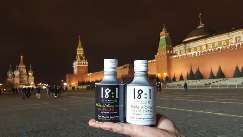 Bidons d'huile d'olive cylindriques blanc et noir de la marque Alexis Muñoz, 18:1, posées sur une main, avec en fond la place Rouge de Moscou, en Russie.