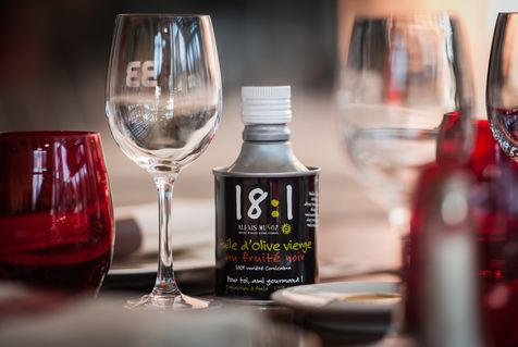 Bidon noir cylindrique d'huile d'olive 18:1, de la marque Alexis Muñoz, sur une table de restaurant.