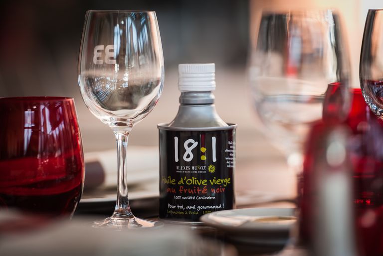 Bidon noir cylindrique d'huile d'olive 18:1, de la marque Alexis Muñoz, sur une table de restaurant.