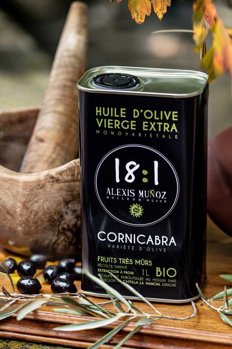 bidon d'huile d'olive noir avec des olives noires et un mortier en bois à coté