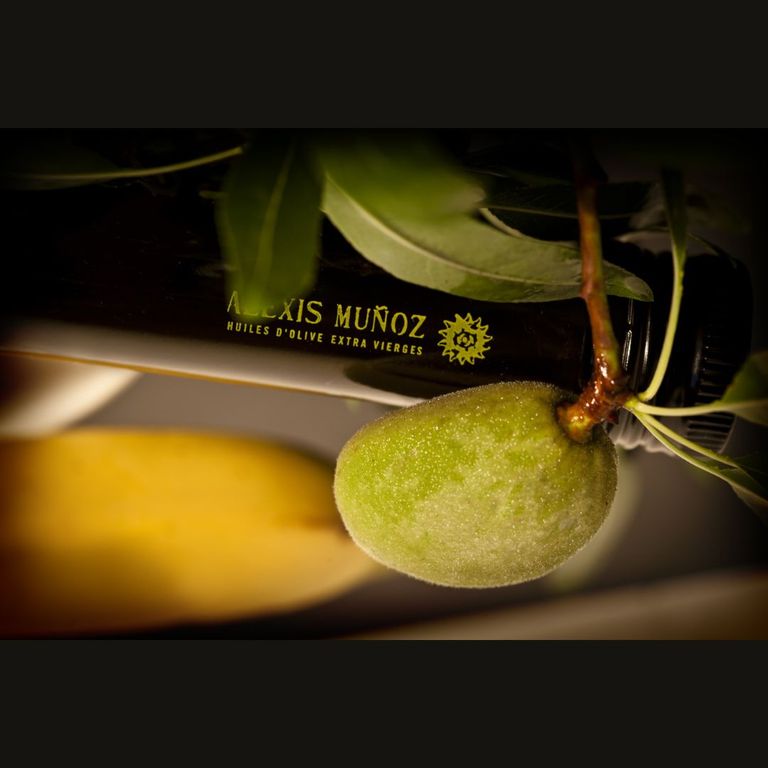 goulot d'une bouteille d'huile d'olive alexis muñoz édition limitée, entourée d'une branche d'olivier, une feuille et une olive verte, sur fond sombre