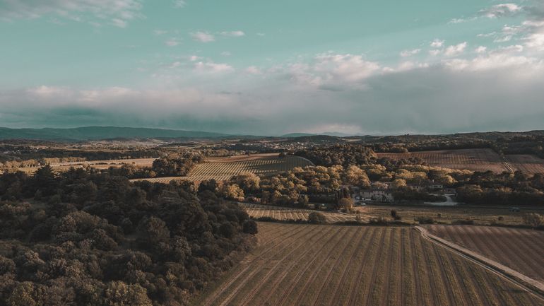 Vue aérienne du domaine de Baudrigue, dans des tons de marrons, vert et un ciel partiellement nuageux, avec une superbe luminosité.