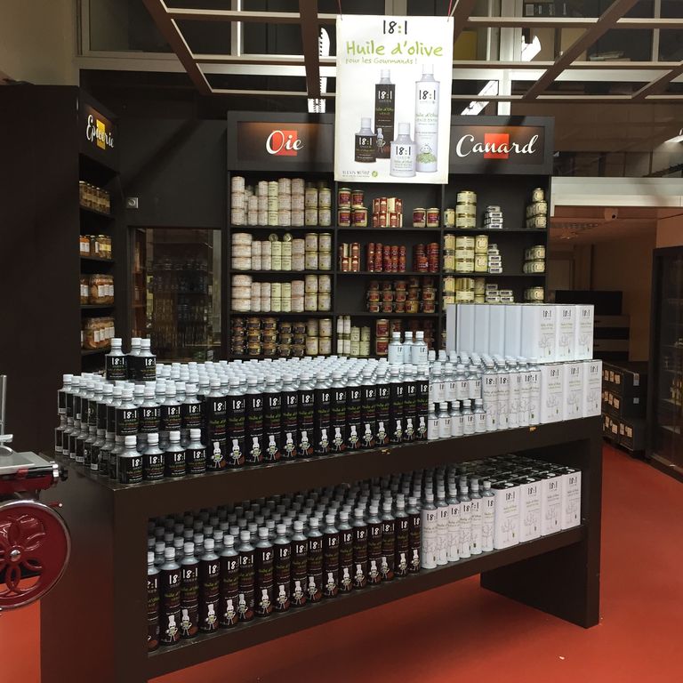 Stand of the distributor Maison Masse, featuring black and white cylindrical cans of 18:1 monovarietal olive oils from the Alexis Muñoz brand.