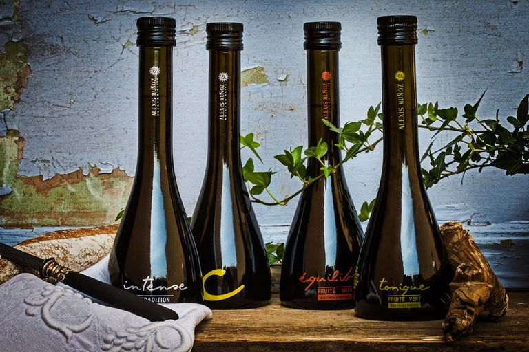 Four 250ml glass bottles, limited editions of olive oils produced by Alexis Muñoz, placed on a wooden table in a rustic setting.